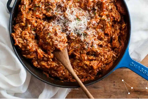 Blue pan sitting on a wooden table with a white table cloth with greek orzo with ground beef