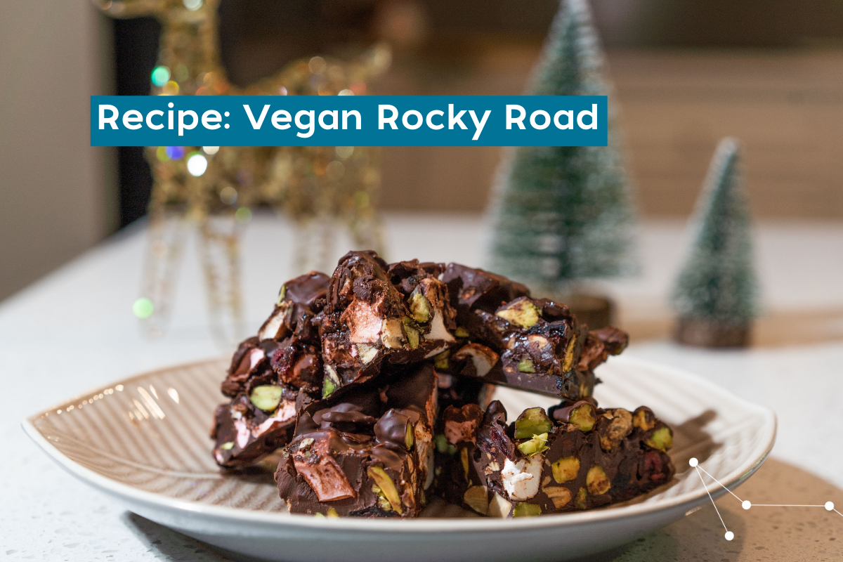 A light brown plate piled with chopped rocky road on a white stone bench with christmas decorations in the background (golden reindeer and two small Christmas trees)