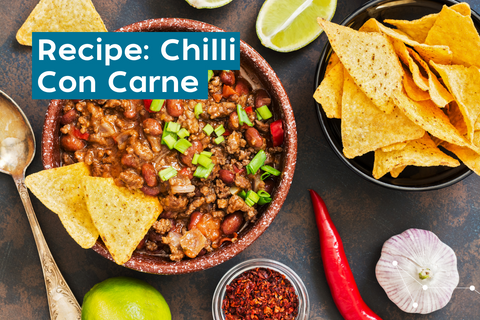 bowl of chilli con carne garnished with spring onions, lime, chilli and corn chips